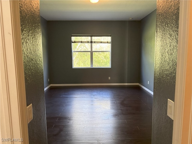 unfurnished room featuring baseboards, dark wood-style flooring, and a textured wall