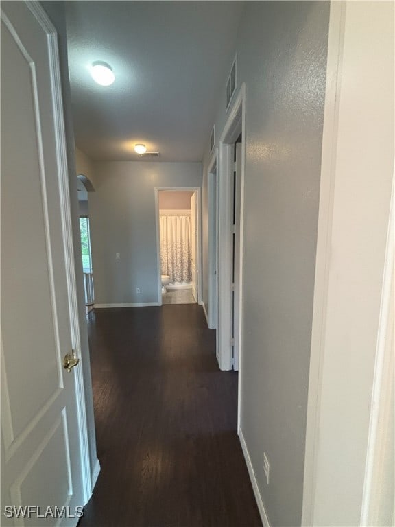 corridor featuring dark wood finished floors, arched walkways, visible vents, and baseboards