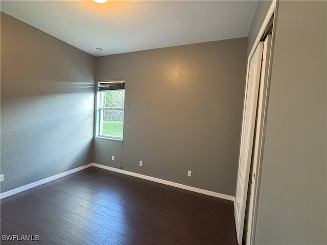 spare room featuring dark wood-type flooring and baseboards