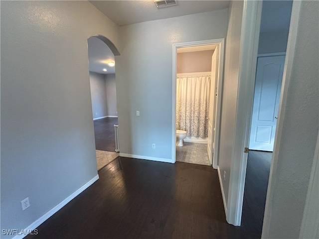 hall featuring dark wood finished floors, visible vents, baseboards, and arched walkways