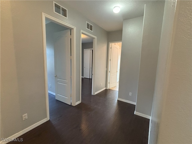 hall with visible vents, baseboards, and dark wood-style flooring