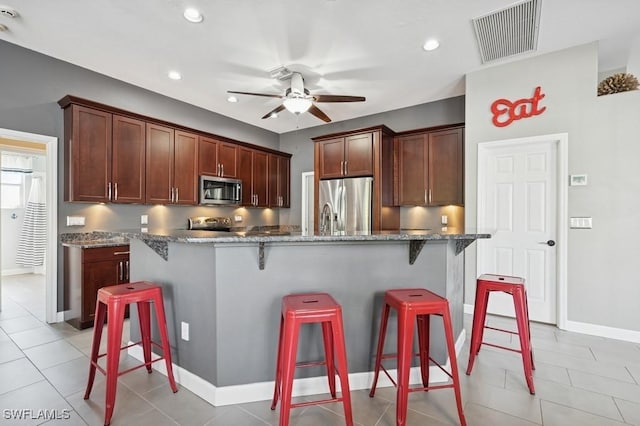 kitchen featuring a breakfast bar area, visible vents, stone countertops, ceiling fan, and appliances with stainless steel finishes