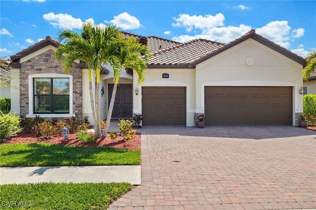 mediterranean / spanish home with stucco siding, a garage, stone siding, a tile roof, and decorative driveway