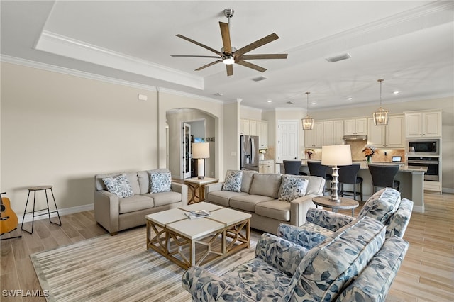 living area with light wood finished floors, visible vents, ceiling fan, arched walkways, and a raised ceiling