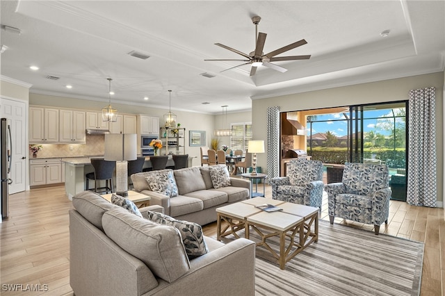 living room with crown molding, a raised ceiling, light wood-type flooring, and ceiling fan