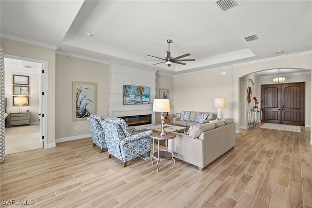 living room featuring wood finish floors, a tray ceiling, arched walkways, and visible vents