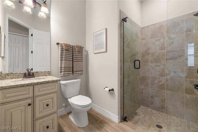 bathroom with a shower stall, baseboards, wood finish floors, toilet, and vanity