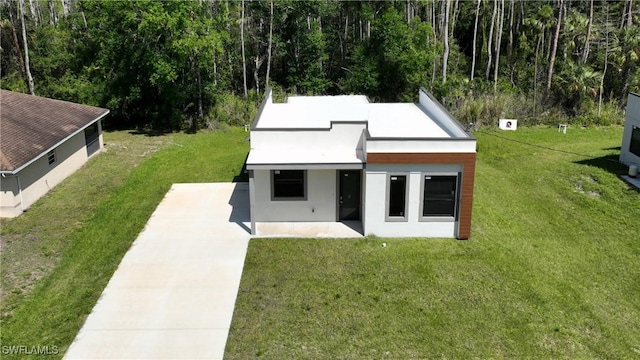 back of house featuring a lawn, driveway, a patio, and stucco siding