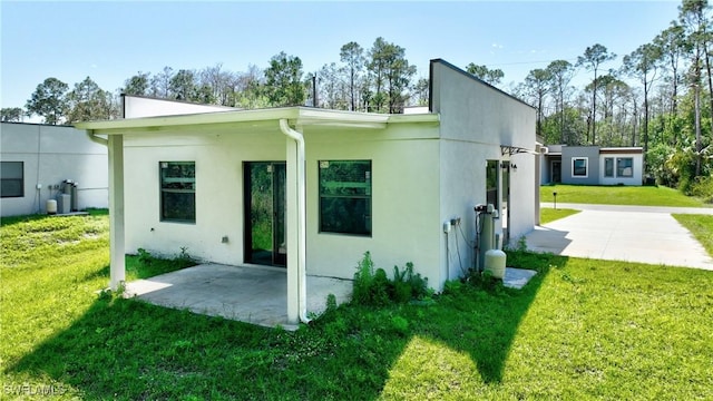back of house featuring a patio area, a lawn, and stucco siding