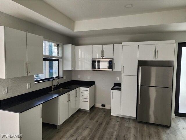 kitchen with wood finished floors, white cabinetry, stainless steel appliances, and a sink