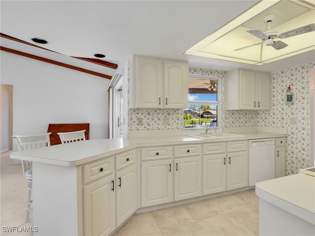 kitchen featuring a ceiling fan, wallpapered walls, a peninsula, white dishwasher, and a sink