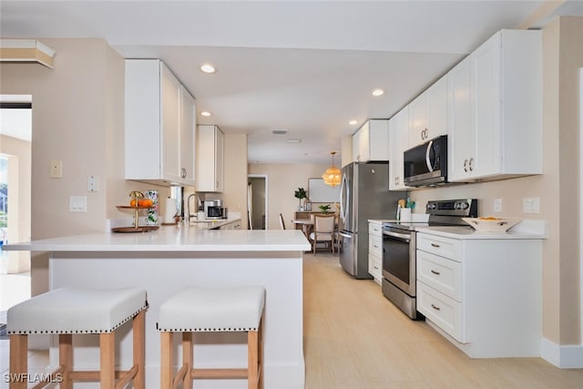 kitchen featuring a breakfast bar, a peninsula, white cabinetry, and appliances with stainless steel finishes