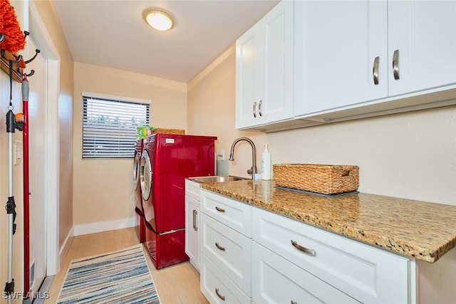 clothes washing area with light wood-style flooring, a sink, cabinet space, separate washer and dryer, and baseboards