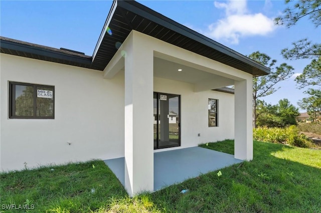 rear view of property featuring a patio area, a lawn, and stucco siding