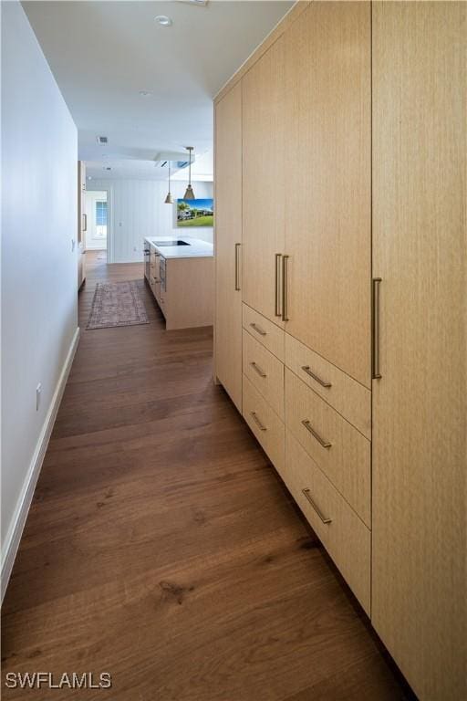 hallway with dark wood finished floors, visible vents, and baseboards