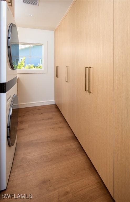 washroom with visible vents, light wood finished floors, stacked washer / dryer, baseboards, and laundry area