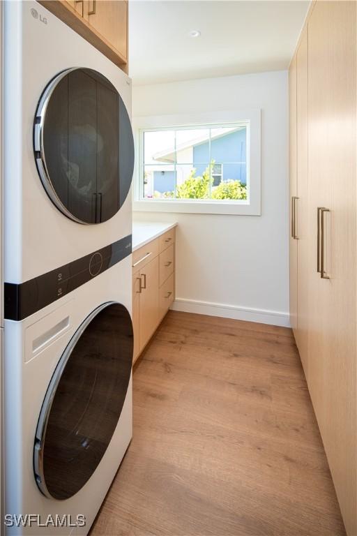 washroom featuring baseboards, cabinet space, stacked washer and clothes dryer, and light wood-style flooring