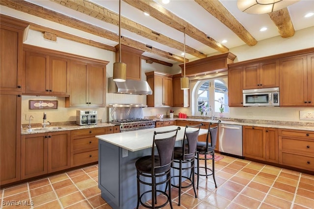 kitchen featuring wall chimney range hood, a breakfast bar area, brown cabinets, appliances with stainless steel finishes, and a sink