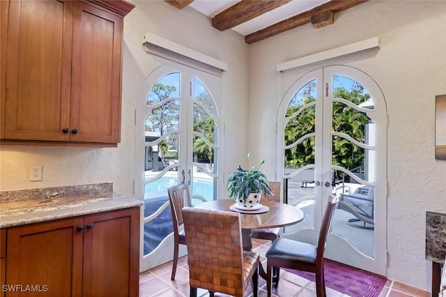 dining room featuring beamed ceiling, light tile patterned floors, french doors, and a textured wall