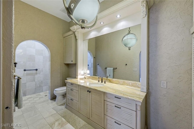 bathroom featuring vanity, toilet, a textured wall, and a tile shower