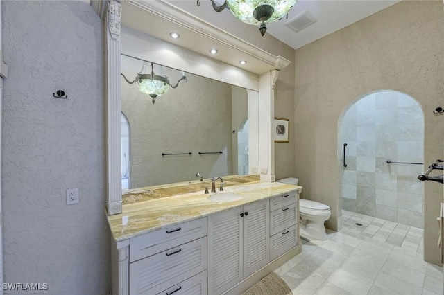 full bath featuring visible vents, toilet, tiled shower, vanity, and a textured wall