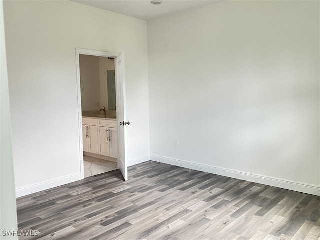 unfurnished bedroom with light wood-style floors, baseboards, ensuite bathroom, and a sink