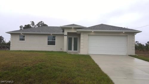 view of front facade with an attached garage, stucco siding, concrete driveway, a front lawn, and french doors