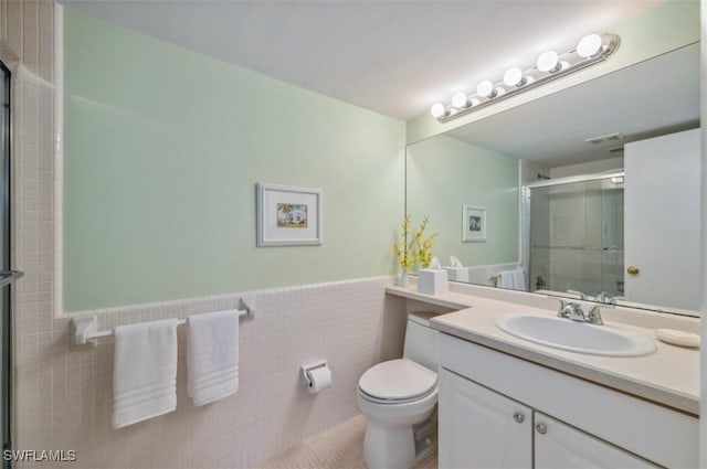 full bathroom with a shower with door, toilet, vanity, wainscoting, and tile walls