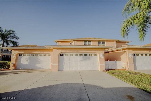 view of front facade with stucco siding, driveway, a gate, fence, and an attached garage