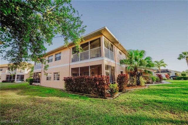 rear view of property featuring a lawn, a sunroom, and stucco siding