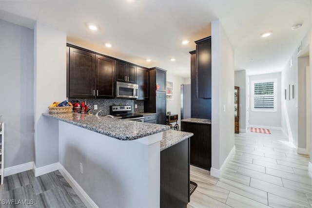 kitchen featuring decorative backsplash, dark brown cabinetry, light stone counters, a peninsula, and stainless steel appliances