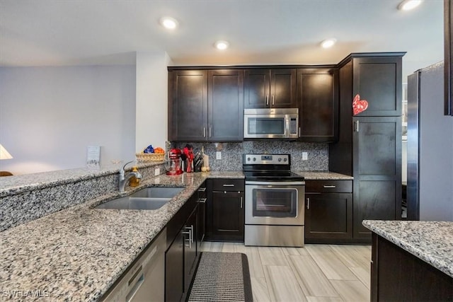 kitchen featuring dark brown cabinets, appliances with stainless steel finishes, light stone counters, a sink, and tasteful backsplash