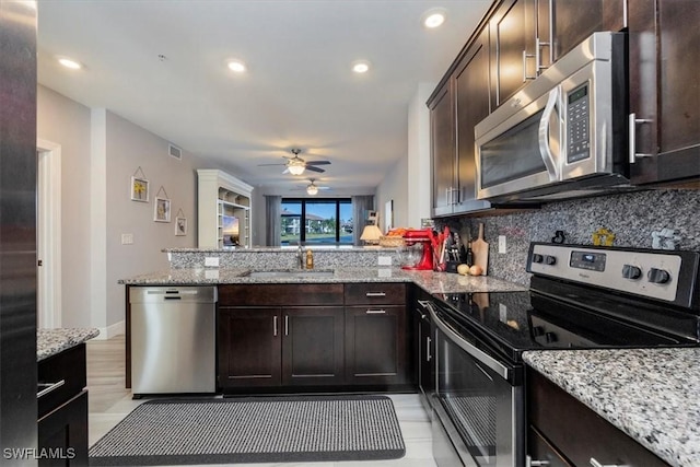 kitchen with a peninsula, dark brown cabinets, tasteful backsplash, a sink, and appliances with stainless steel finishes