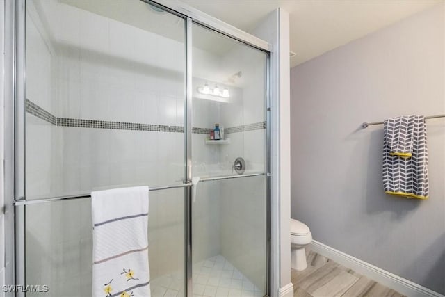 full bath featuring baseboards, a stall shower, toilet, and wood finished floors