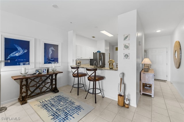 kitchen with a kitchen breakfast bar, light tile patterned floors, stainless steel refrigerator with ice dispenser, and white cabinets