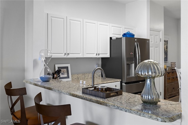 kitchen featuring a kitchen bar, light stone counters, white cabinets, stainless steel fridge, and a sink