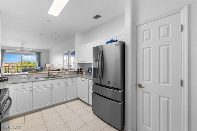 kitchen featuring visible vents, a sink, stove, white cabinets, and stainless steel fridge