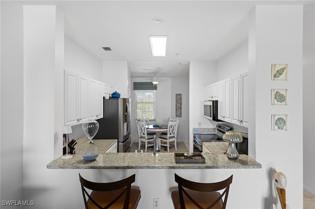 kitchen with a breakfast bar area, visible vents, a peninsula, white cabinets, and appliances with stainless steel finishes