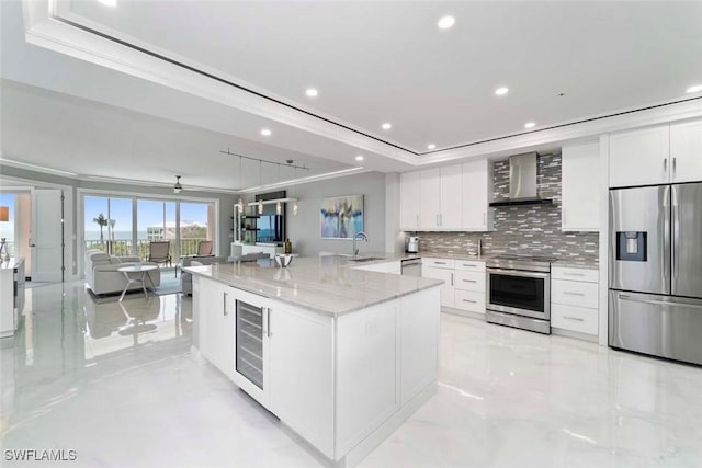 kitchen featuring beverage cooler, a tray ceiling, stainless steel appliances, white cabinetry, and wall chimney range hood