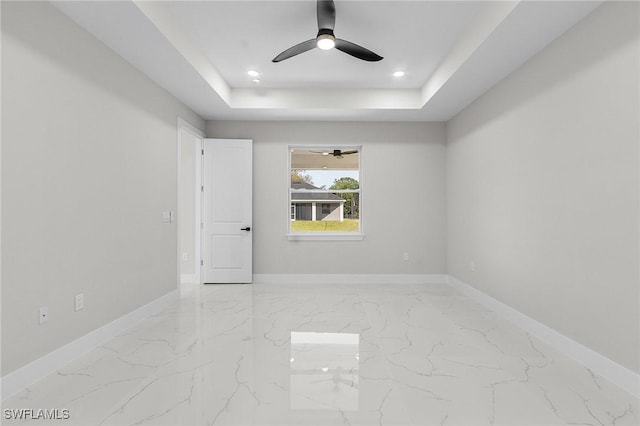 spare room featuring marble finish floor, baseboards, a tray ceiling, and a ceiling fan