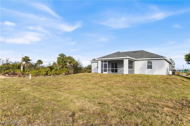 back of property with stucco siding, a lawn, roof with shingles, and a sunroom