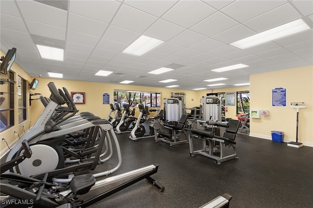 exercise room featuring a paneled ceiling and baseboards