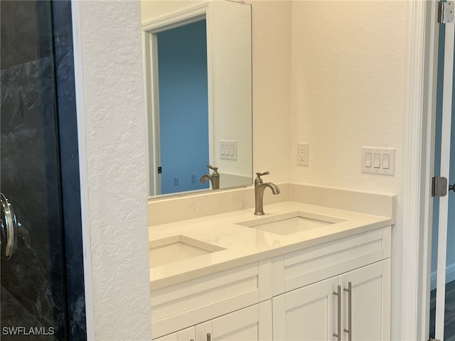 full bath with a sink, double vanity, and a textured wall