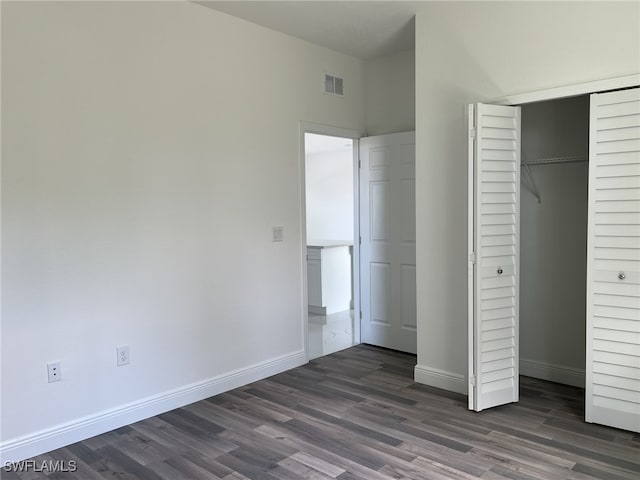 unfurnished bedroom featuring dark wood-style flooring, baseboards, visible vents, and a closet