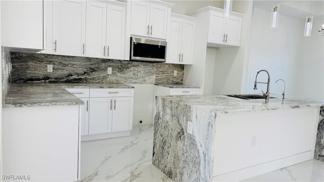 kitchen featuring stainless steel microwave, light stone counters, marble finish floor, white cabinetry, and a sink