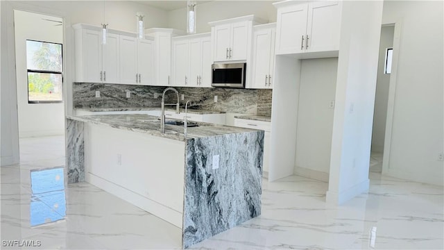 kitchen featuring marble finish floor, a sink, stainless steel microwave, light stone counters, and backsplash