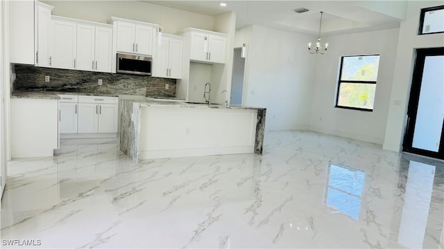 kitchen with a notable chandelier, marble finish floor, stainless steel microwave, white cabinets, and decorative backsplash