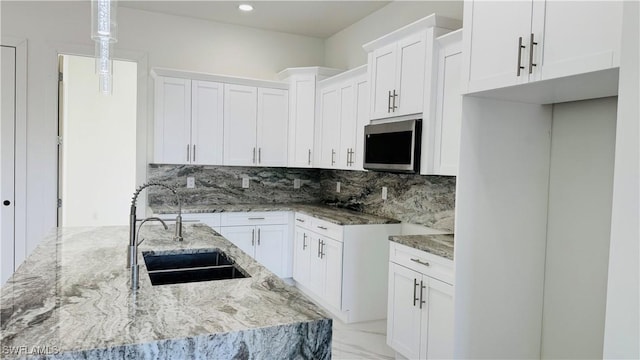 kitchen featuring a sink, stainless steel microwave, light stone counters, and backsplash