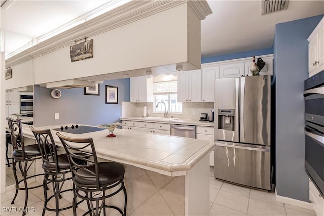 kitchen with visible vents, tile countertops, a breakfast bar area, appliances with stainless steel finishes, and a sink