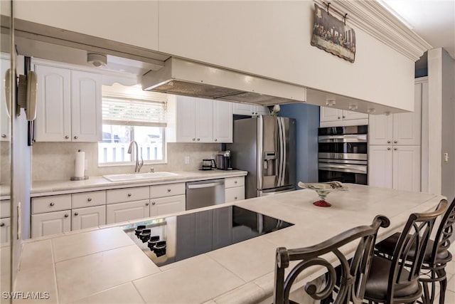 kitchen with a breakfast bar, a sink, light countertops, white cabinets, and appliances with stainless steel finishes